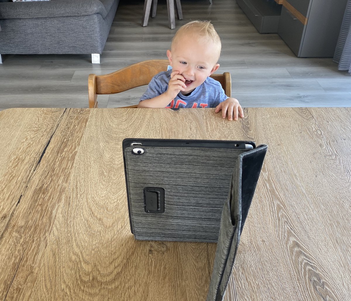 Baby lachend auf einem Hochstuhl. Es schaut auf den Bildschirm eines iPads.